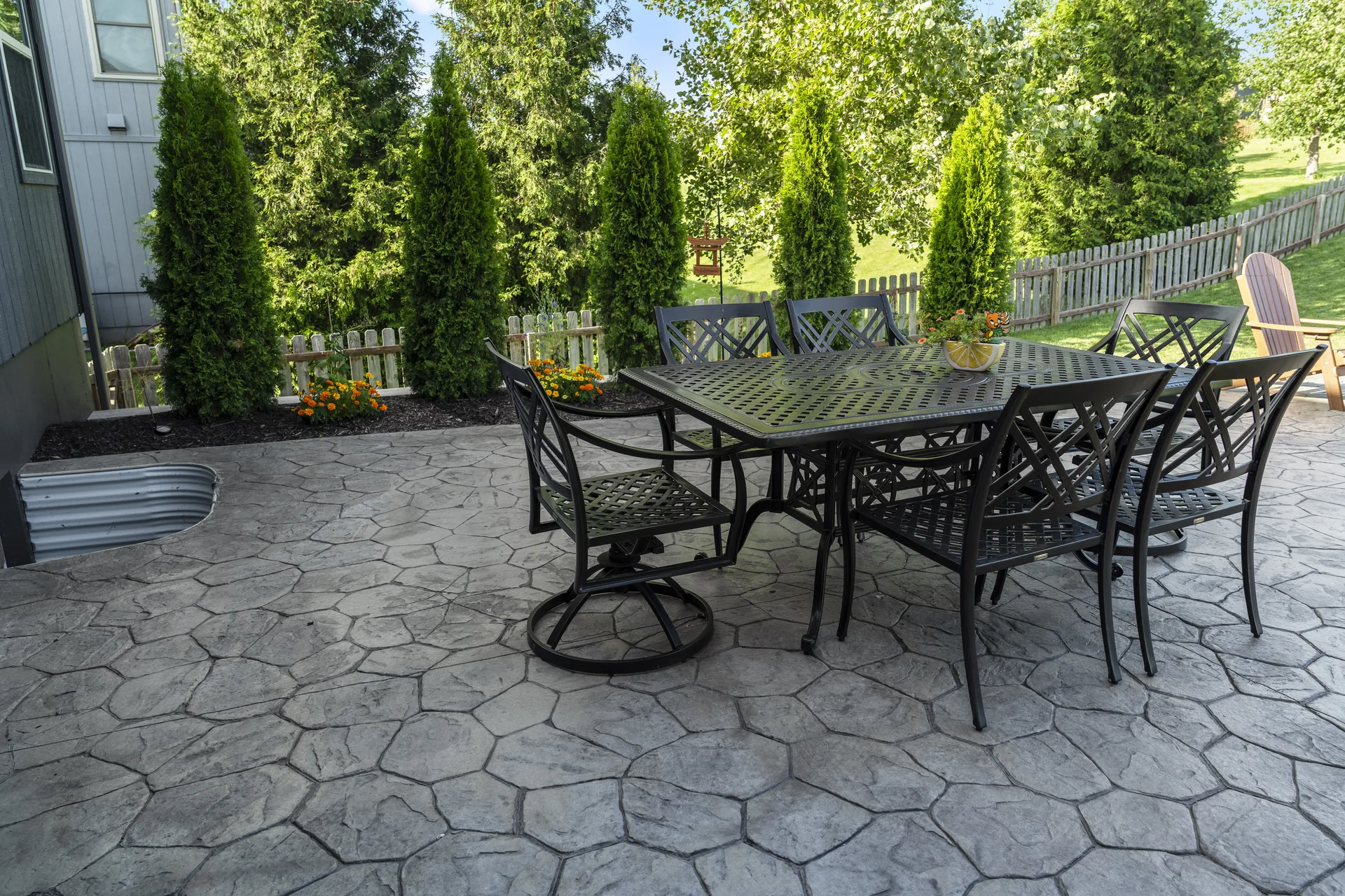 Outdoor dining table on the pavers beside a row of evergreens