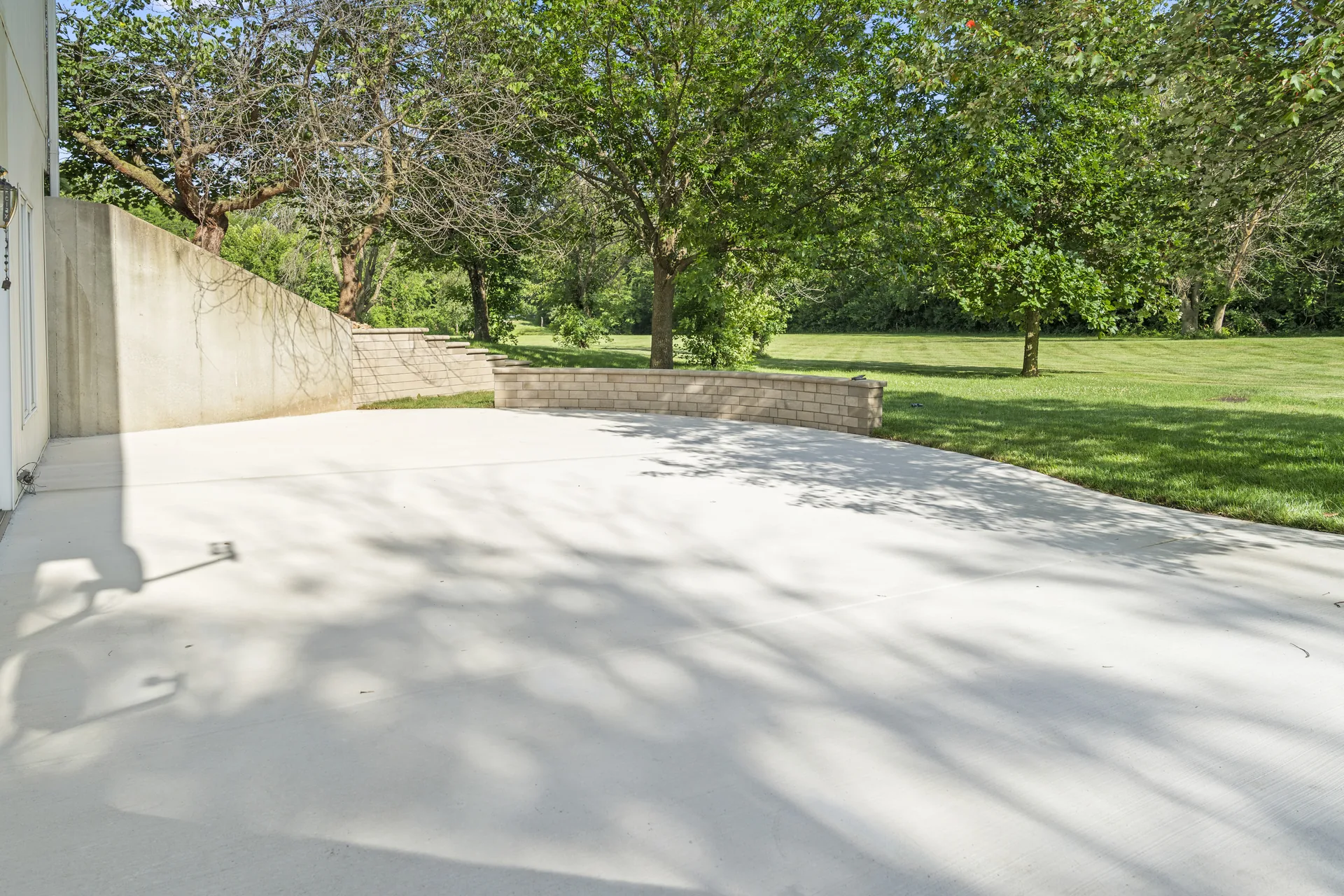 Concrete patio framed by shade trees and a retaining wall