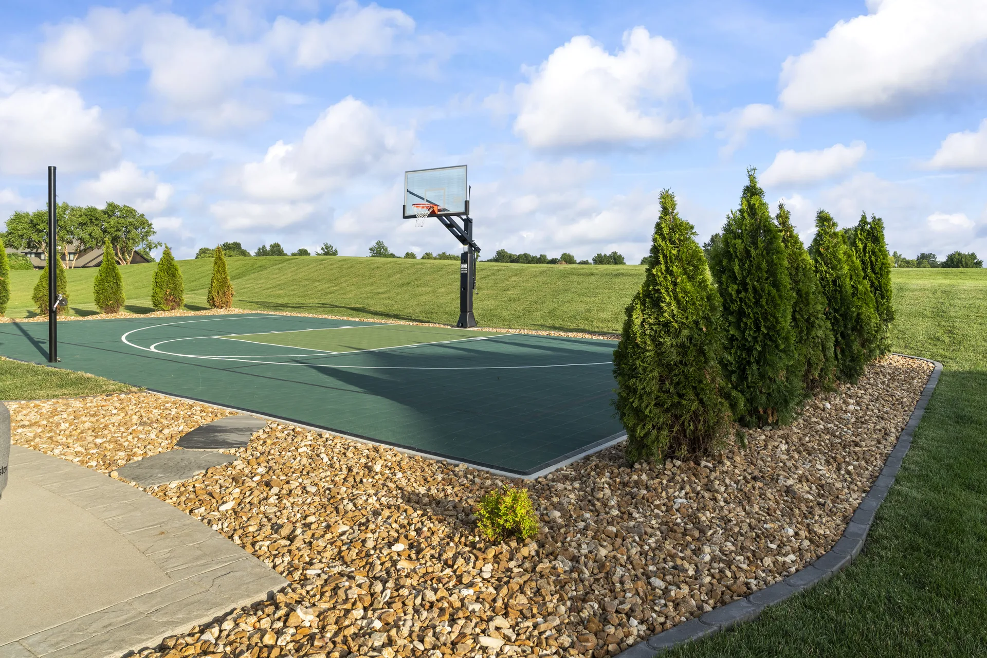 Sport court edge next to a stone-and-mulch planting bed