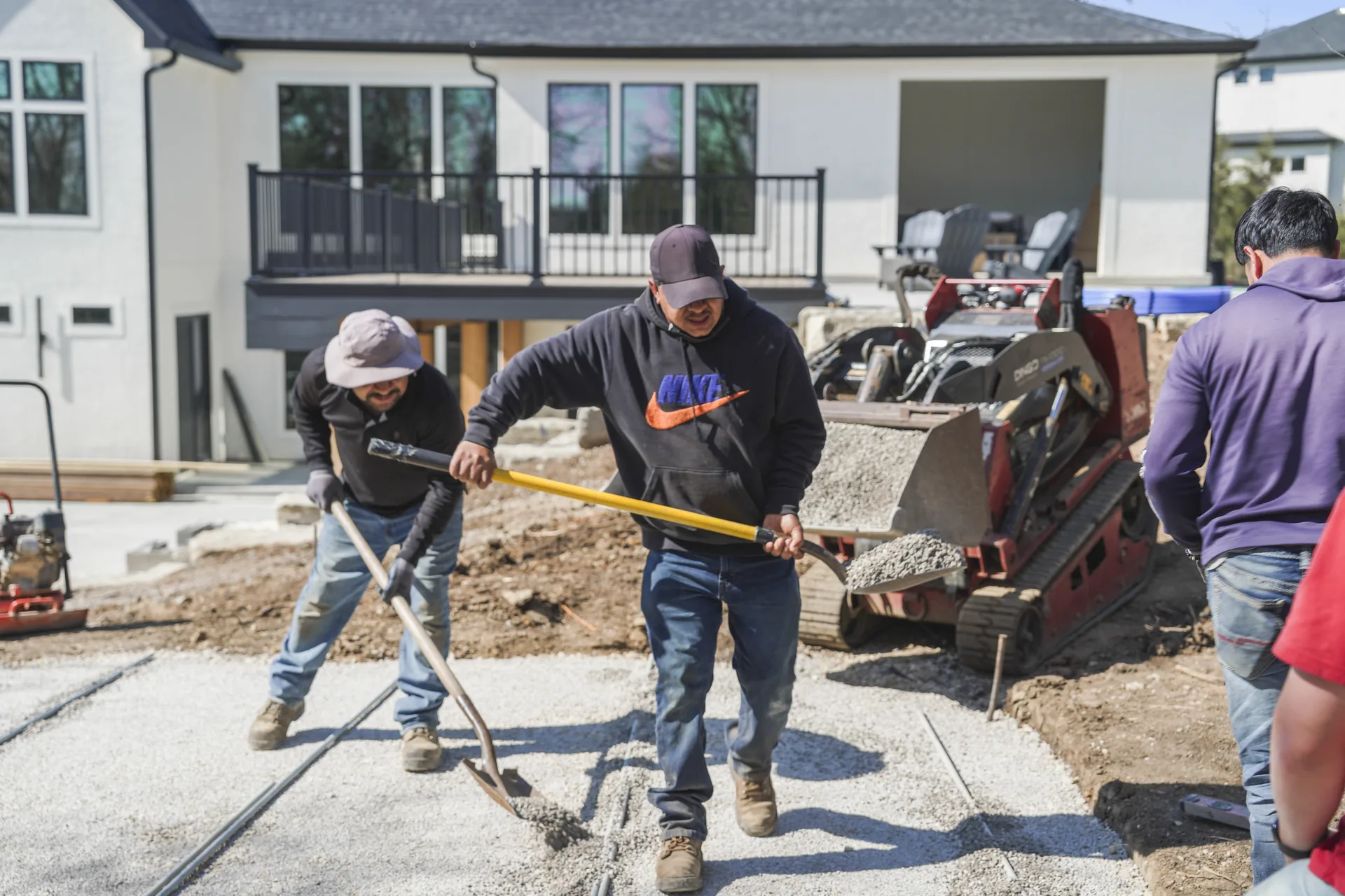 Workers fitting individual pavers near the house